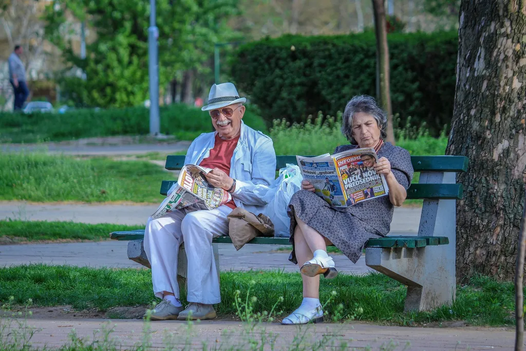 Seniorenpaar sitzt gemeinsam auf einer Parkbank und liest Zeitung – 65 Jahre – Sprüche zum 65. Geburtstag und zum Ruhestand