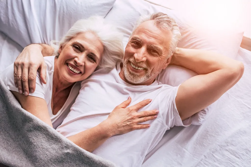 Älteres Ehepaar liegt lächelnd nebeneinander zuhause im Bett – Goldene Hochzeit – Sprüche und Glückwünsche zum 50. Hochzeitstag