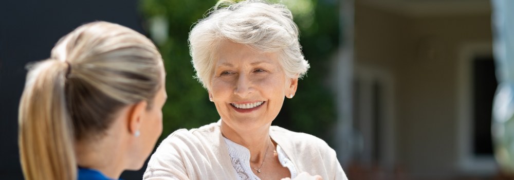 Frau mit weißem Oberteil lacht ihre Pflegerin an